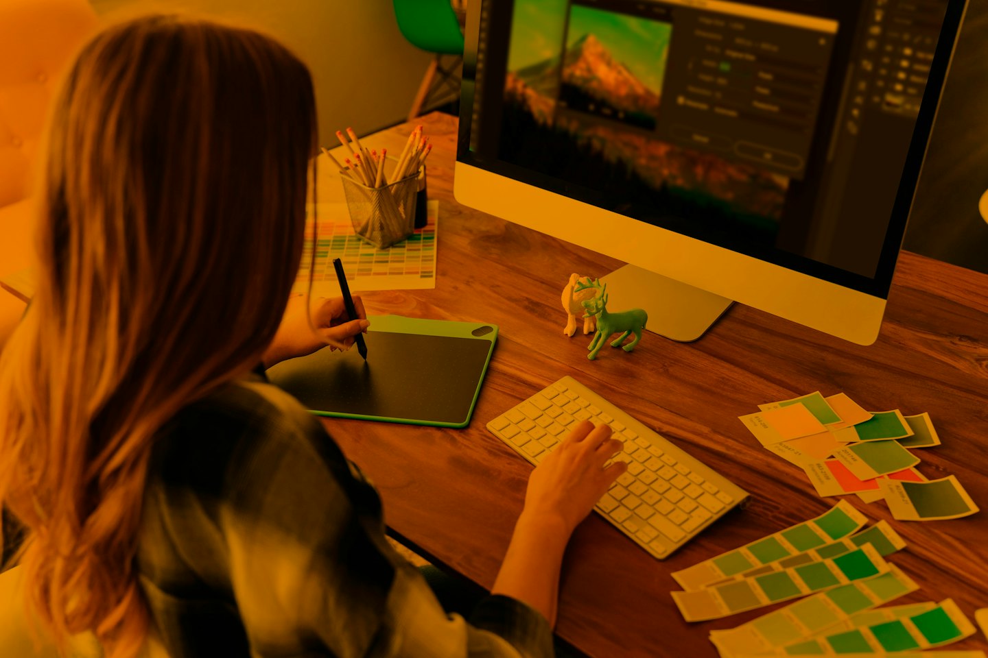 Grafikdesigner bearbeitet Bild am Computer mit Tablet und Tastatur.